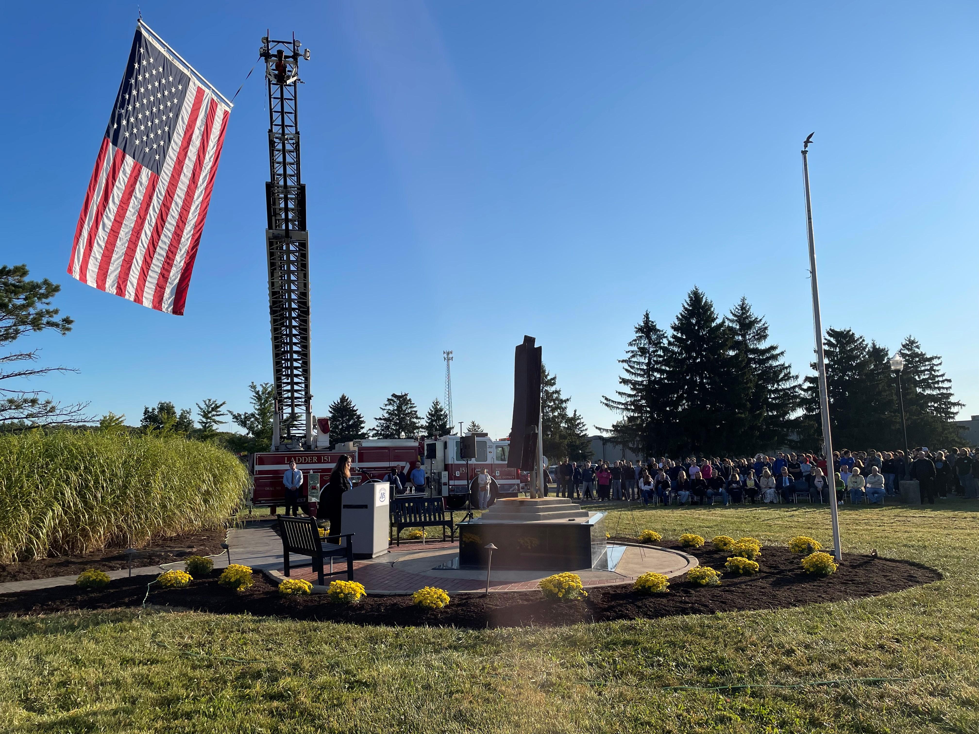 Crowd around the LCJVS Patriot Day Memorial with USA flag flying in background